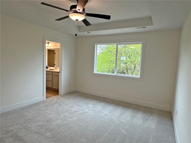 unfurnished bedroom with light carpet, ensuite bath, a raised ceiling, and ceiling fan