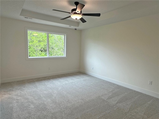 carpeted spare room featuring a raised ceiling and ceiling fan