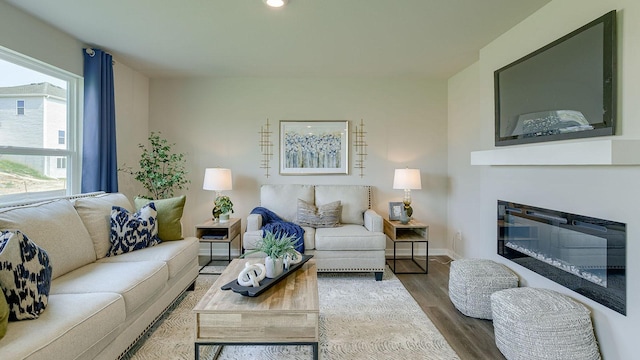 living area featuring a glass covered fireplace, recessed lighting, wood finished floors, and baseboards