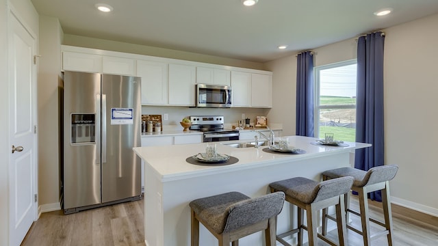 kitchen featuring a kitchen island with sink, light hardwood / wood-style flooring, stainless steel appliances, sink, and white cabinets