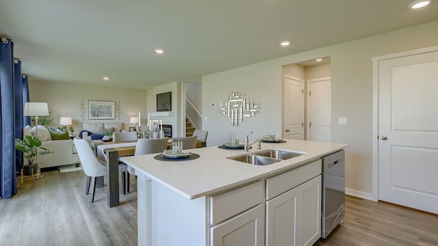 kitchen with dishwasher, light hardwood / wood-style floors, an island with sink, sink, and white cabinetry