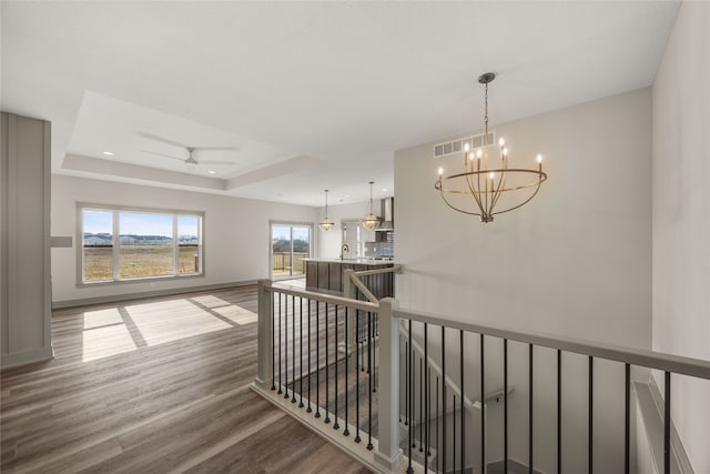 hall featuring hardwood / wood-style flooring, plenty of natural light, a raised ceiling, and a notable chandelier