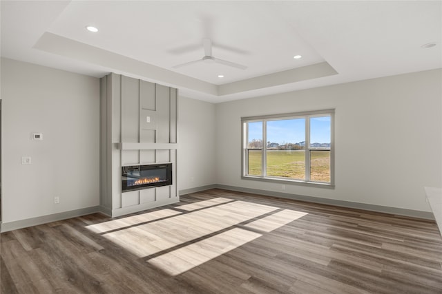 unfurnished living room featuring hardwood / wood-style floors, a large fireplace, ceiling fan, and a raised ceiling