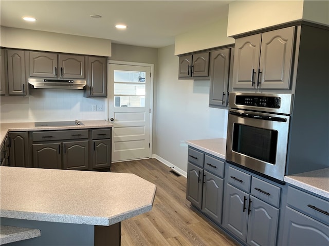 kitchen with black electric stovetop, gray cabinetry, backsplash, oven, and light wood-type flooring