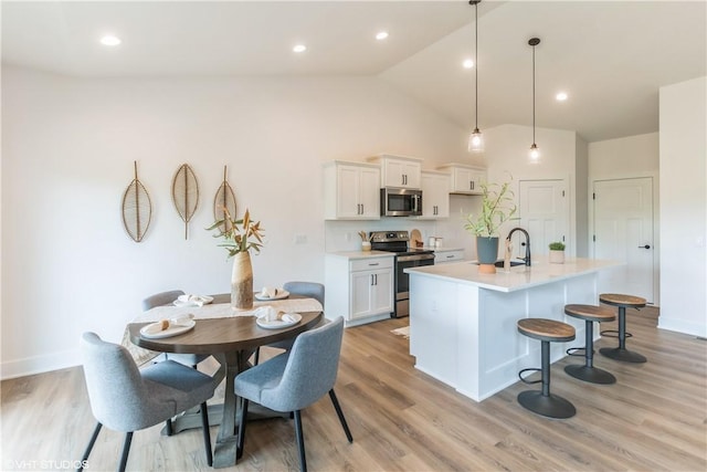 kitchen with white cabinetry, hanging light fixtures, stainless steel appliances, an island with sink, and vaulted ceiling