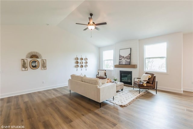 living room with a large fireplace, vaulted ceiling, ceiling fan, and dark wood-type flooring