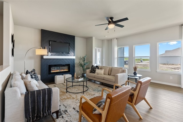 living room featuring ceiling fan, a large fireplace, and wood-type flooring