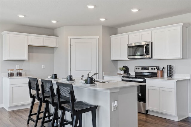 kitchen with stainless steel appliances, a kitchen island with sink, sink, white cabinets, and dark hardwood / wood-style floors