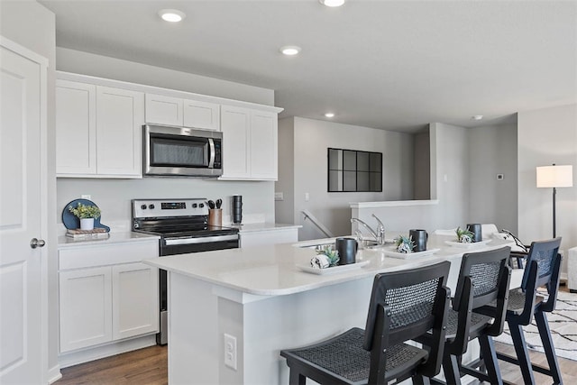 kitchen featuring hardwood / wood-style floors, stainless steel appliances, white cabinetry, and an island with sink