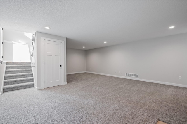 basement featuring light colored carpet and a textured ceiling