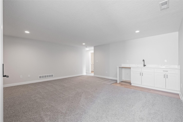 interior space with a textured ceiling, light colored carpet, and sink