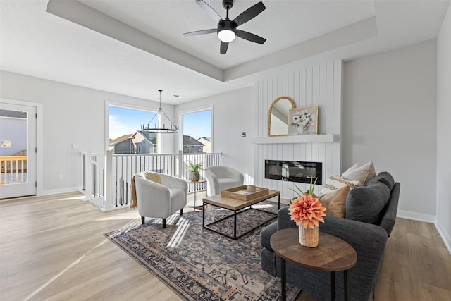 living room featuring a raised ceiling, a large fireplace, hardwood / wood-style floors, and ceiling fan with notable chandelier