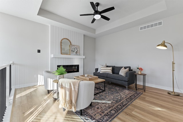 living room featuring a fireplace, a tray ceiling, light hardwood / wood-style flooring, and ceiling fan