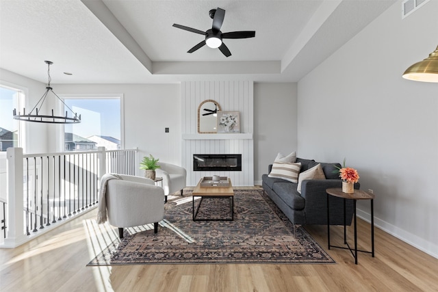 living room featuring a tray ceiling, ceiling fan with notable chandelier, and hardwood / wood-style flooring