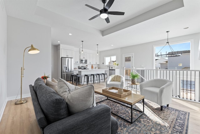 living room featuring a raised ceiling, ceiling fan, and light hardwood / wood-style flooring