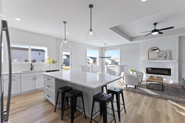 kitchen with white cabinetry, sink, a center island, hanging light fixtures, and light wood-type flooring