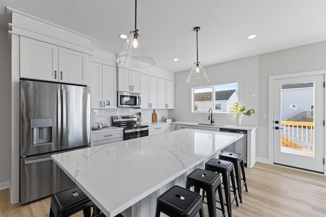 kitchen with stainless steel appliances, sink, white cabinetry, a kitchen island, and hanging light fixtures