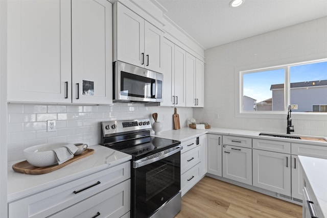 kitchen featuring sink, appliances with stainless steel finishes, light hardwood / wood-style floors, light stone counters, and white cabinetry