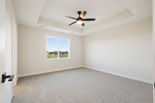 carpeted empty room with a raised ceiling and ceiling fan