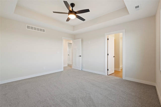 unfurnished bedroom featuring connected bathroom, light colored carpet, ceiling fan, and a tray ceiling