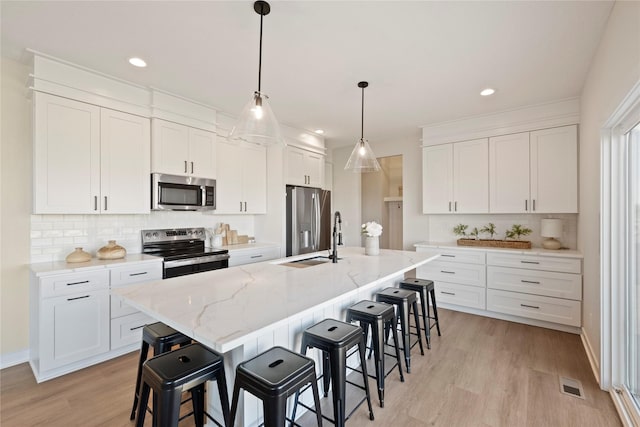 kitchen featuring stainless steel appliances, white cabinetry, sink, and a center island with sink