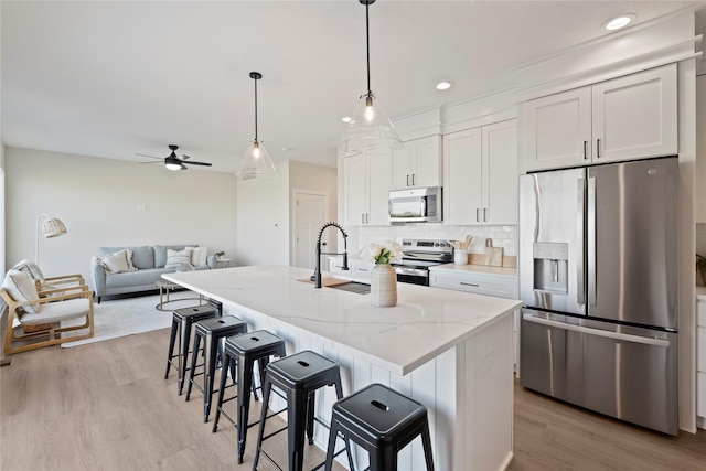 kitchen featuring white cabinetry, stainless steel appliances, light stone counters, and a center island with sink