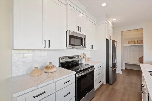 kitchen featuring stainless steel appliances, light stone countertops, light hardwood / wood-style floors, white cabinets, and decorative backsplash