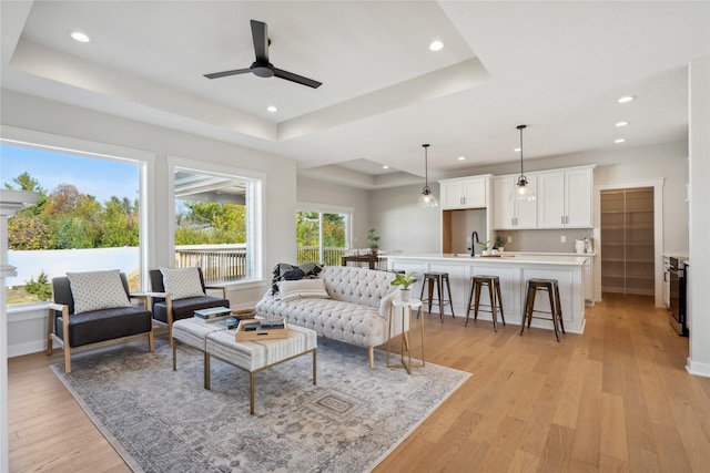 living room with sink, light hardwood / wood-style flooring, a raised ceiling, and ceiling fan