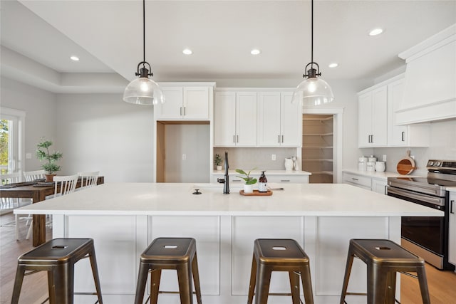 kitchen with white cabinetry, decorative light fixtures, an island with sink, and stainless steel electric range