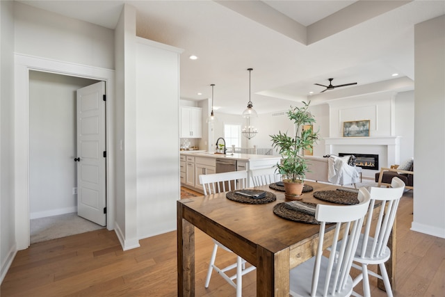 dining room featuring a raised ceiling, sink, ceiling fan with notable chandelier, and light hardwood / wood-style flooring