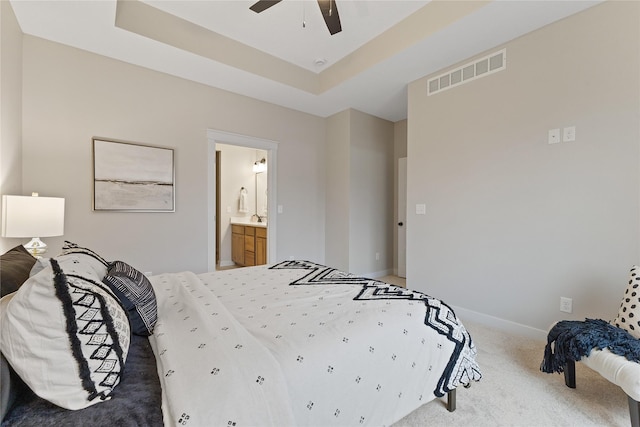 carpeted bedroom with a tray ceiling, ceiling fan, and ensuite bathroom