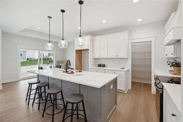 kitchen featuring stainless steel electric stove, sink, pendant lighting, a center island with sink, and white cabinets