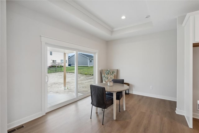 dining area with a raised ceiling and wood-type flooring