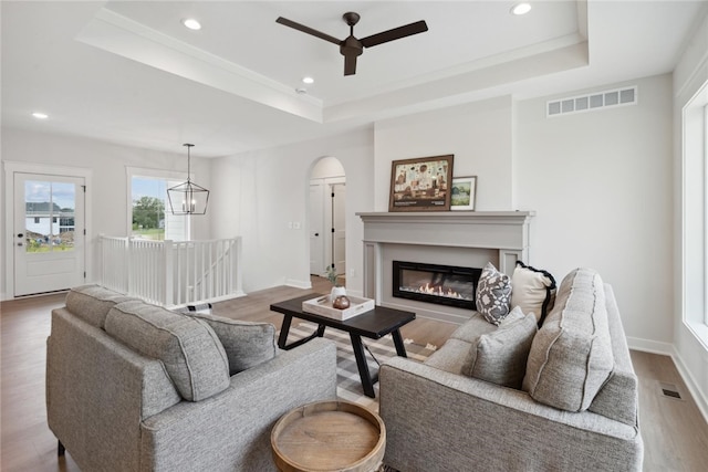 living room with a tray ceiling, hardwood / wood-style floors, and ceiling fan with notable chandelier