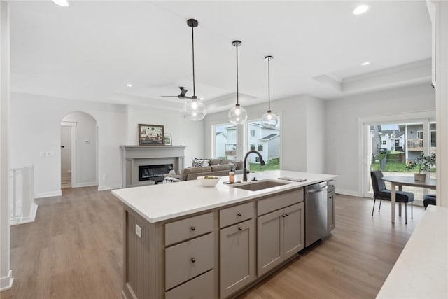 kitchen with stainless steel dishwasher, a raised ceiling, sink, light hardwood / wood-style flooring, and an island with sink