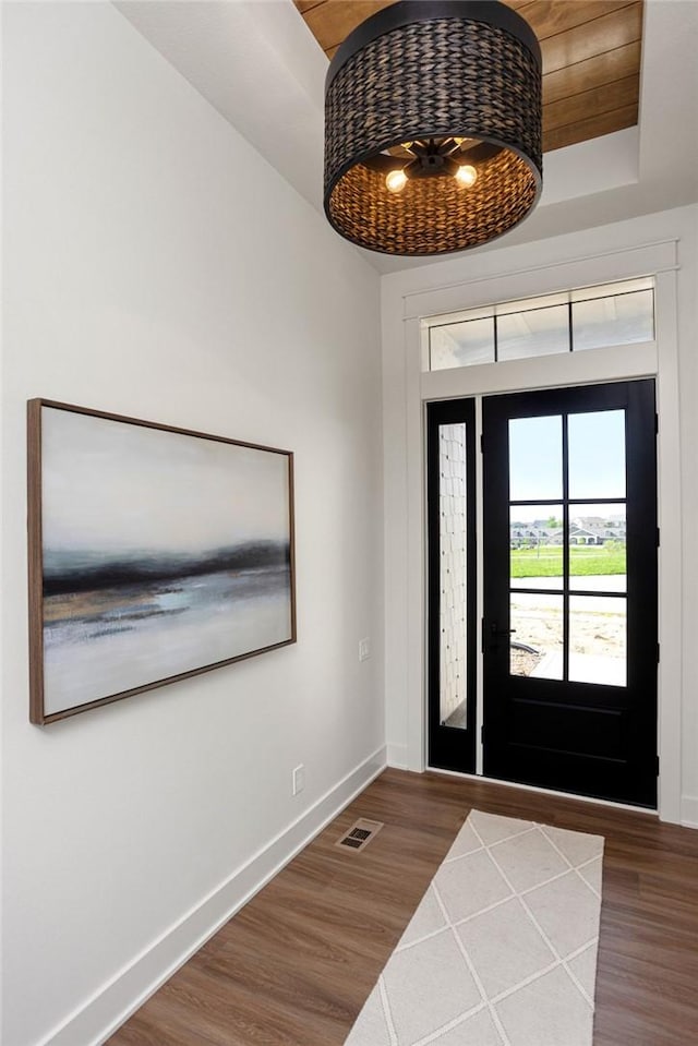 foyer entrance featuring a tray ceiling, baseboards, visible vents, and dark wood-type flooring