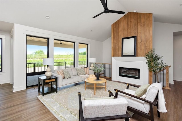 living area featuring a glass covered fireplace, ceiling fan, lofted ceiling, and wood finished floors