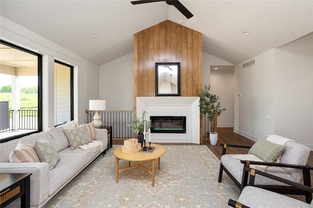 living room with a fireplace, lofted ceiling, visible vents, wood finished floors, and baseboards