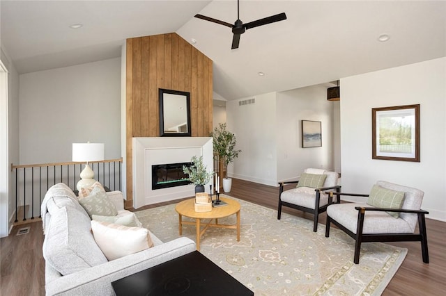 living area featuring vaulted ceiling, a large fireplace, ceiling fan, and wood finished floors