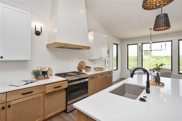 kitchen featuring decorative backsplash, stainless steel range with gas stovetop, custom exhaust hood, light countertops, and a sink