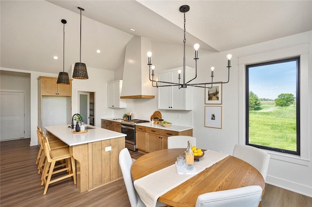 kitchen with lofted ceiling, wood finished floors, wall chimney range hood, stainless steel gas range, and an island with sink