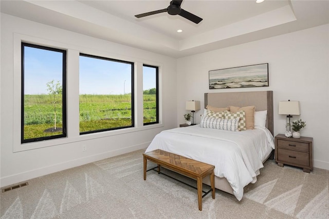 bedroom with baseboards, visible vents, a raised ceiling, and light colored carpet