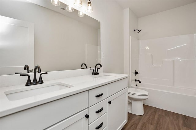 bathroom with toilet, double vanity, a sink, and wood finished floors