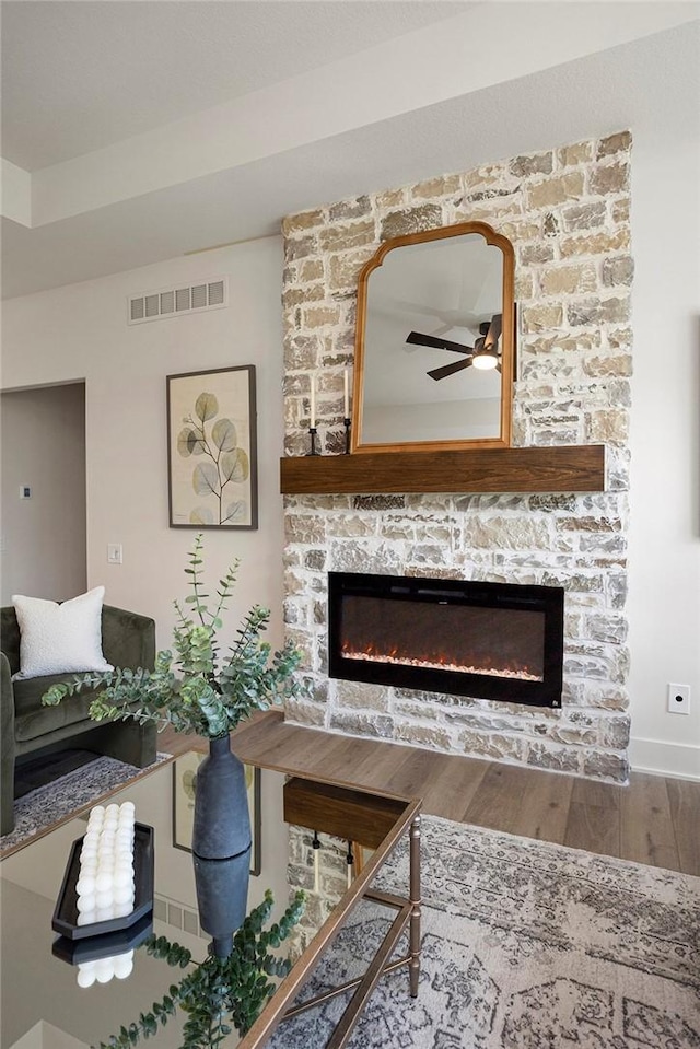 living room with ceiling fan, a stone fireplace, and wood-type flooring