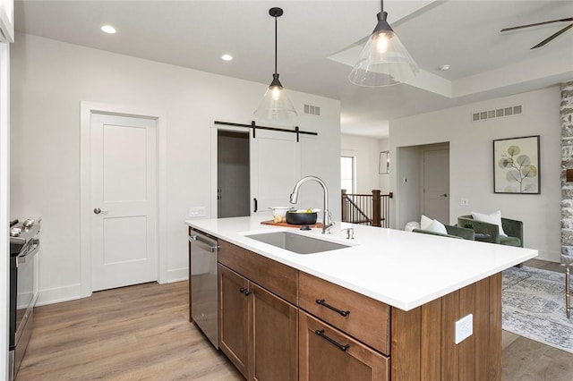 kitchen with a barn door, sink, an island with sink, and stainless steel appliances