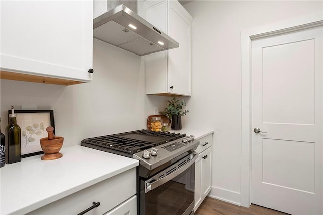 kitchen with hardwood / wood-style flooring, wall chimney exhaust hood, white cabinetry, and stainless steel range with gas stovetop