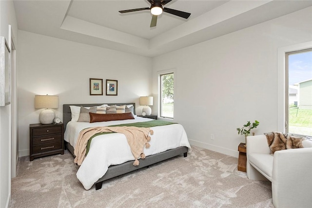 bedroom with light carpet, a tray ceiling, and ceiling fan