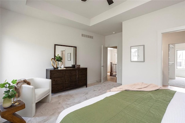 carpeted bedroom with ceiling fan, a raised ceiling, and ensuite bath