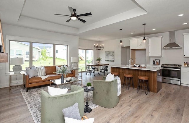 living room with a tray ceiling, ceiling fan with notable chandelier, and light wood-type flooring