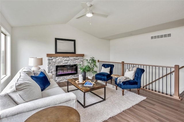 living room featuring vaulted ceiling, a stone fireplace, ceiling fan, and hardwood / wood-style floors